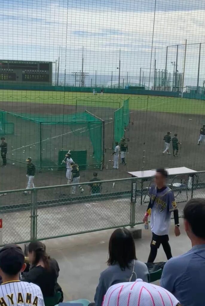 メイン球場のスタンドから、ネット越しに打撃練習を見た様子。選手たちが遠くで練習している（お客さんの顔はモザイク）
