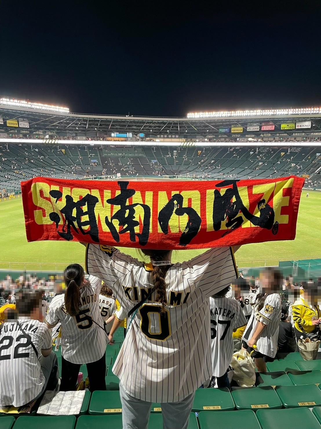 ナイターの甲子園のライトスタンドで、湘南乃風のタオルを広げる後ろ姿